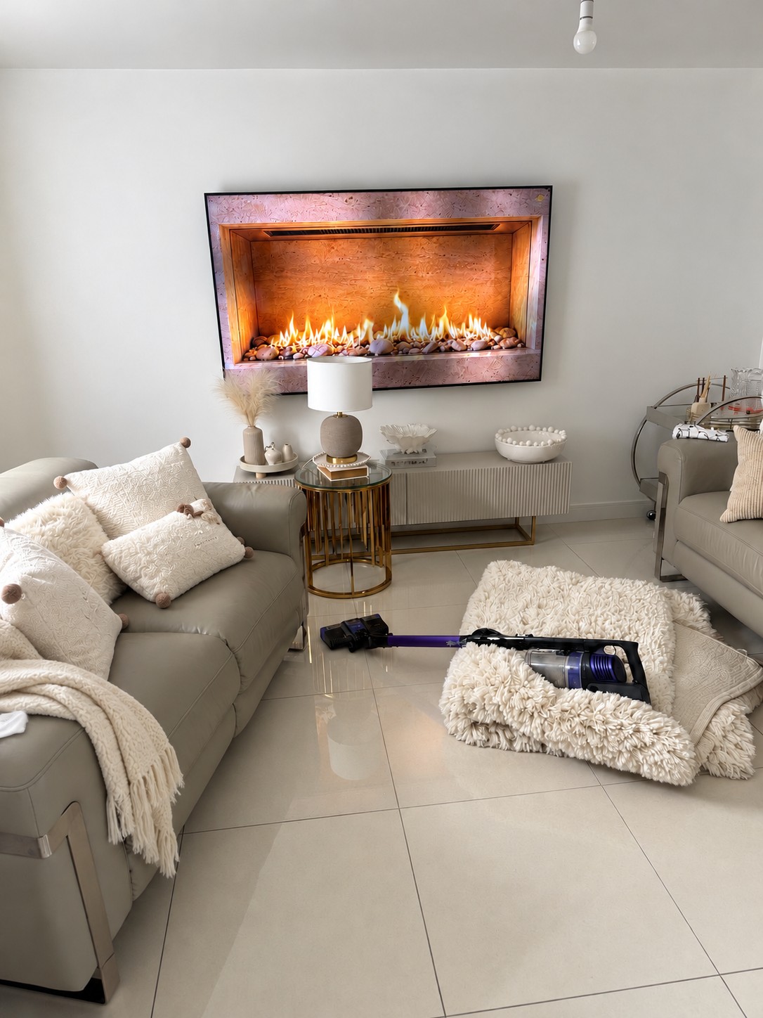 Digitally styled before view with a folded ivory rug, vacuum and slightly untidy cushions